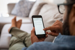 A brown man with glasses interacts with his mobile phone