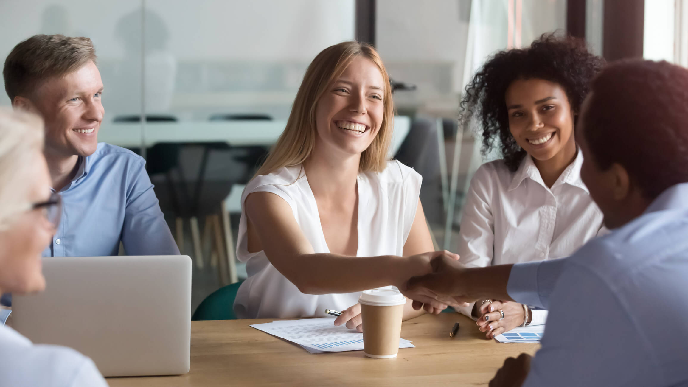 Happy caucasian manager and african client handshaking at group meeting