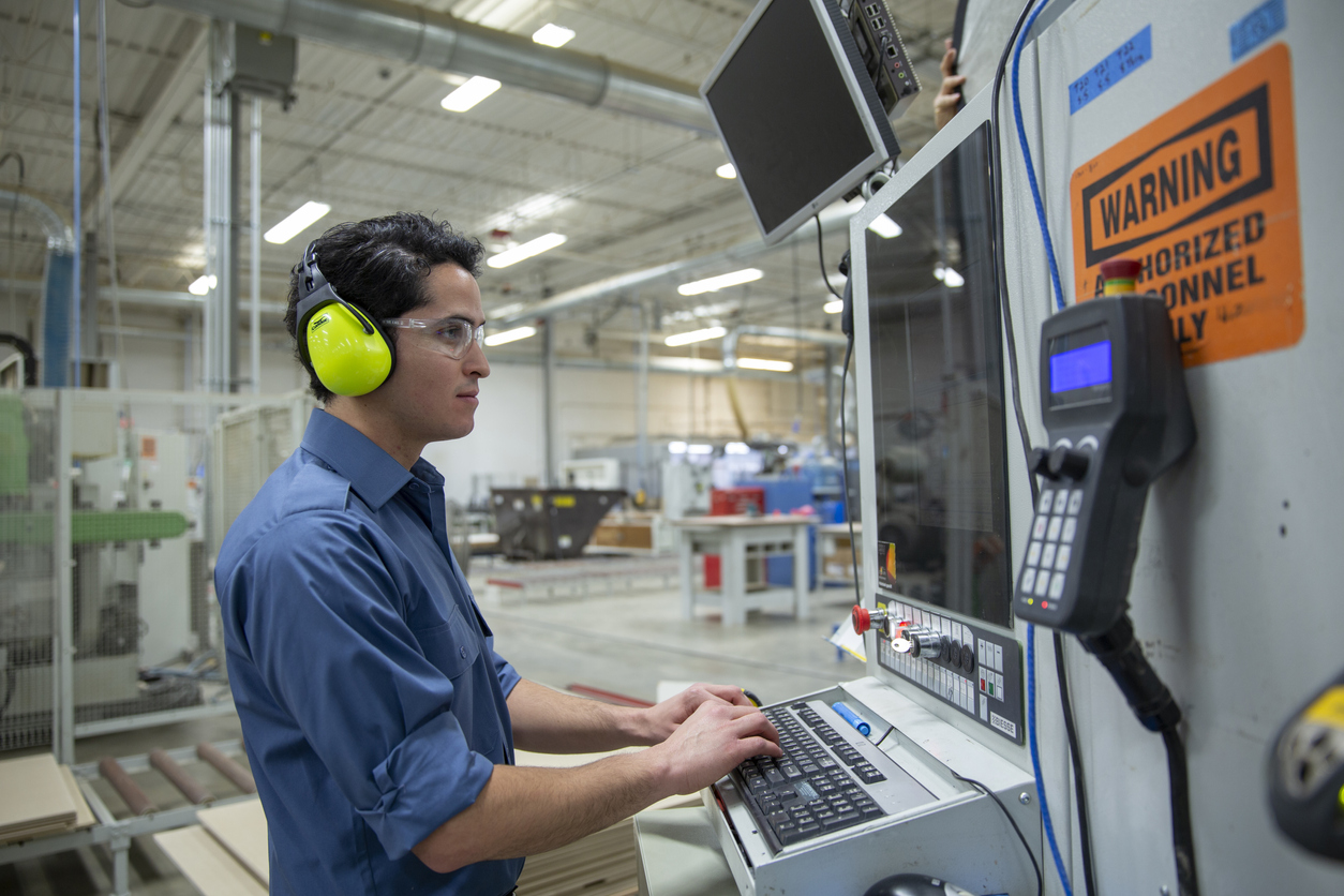 Male worker in ear protectors working at computer in factory