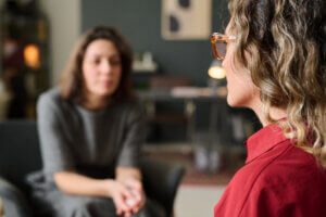 Two women engaging in a one-on-one counseling session in a cozy, well-lit room, one expressing herself while the other listens attentively. The listener demonstrates UX research empathy