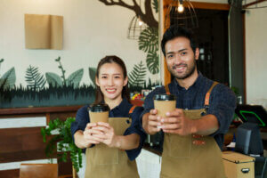 two asian cafe workers offer coffee in welcome gesture