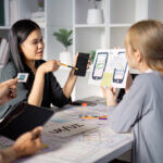 An Asian female UX designer discusses mobile app prototypes, as a white female dev listens.