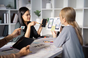 An Asian female UX designer discusses mobile app prototypes, as a white female dev listens.